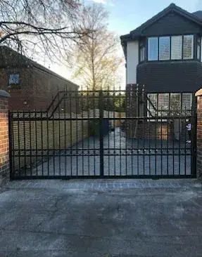 Black metal double gates across a driveway in front of a detached house