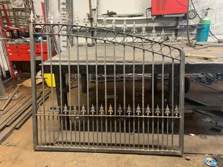 Metal gate with scrollwork and finials standing in the workshop