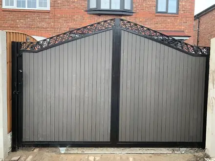 Grey vertical-board double driveway gates with arched black scrollwork between brick pillars