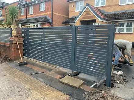 Grey horizontal slatted gates being fitted, with a worker kneeling beside them